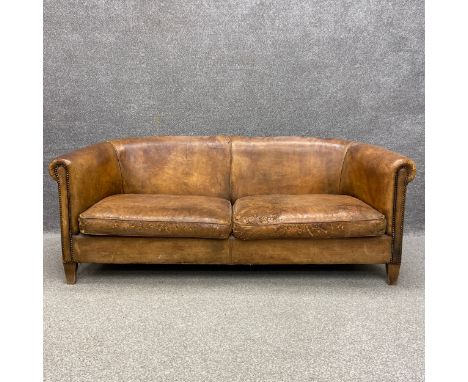 A mid century distressed tan leather Chesterfield style sofa having a scrolled back and arms with stud work detailing over a 