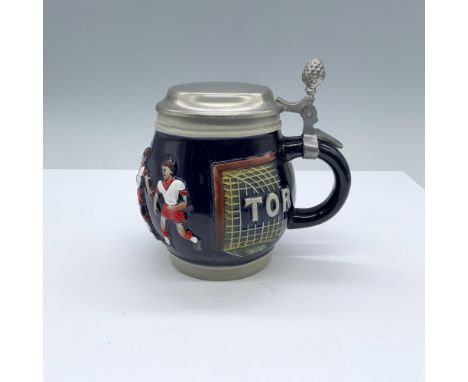 A round ceramic drinking vessel with a high relief depicting boys playing soccer and the words Schuss and Tor over the nets a