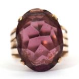 A gemset ring, the oval purple faceted stone in a four claw mount with tapered split shoulders and