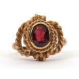 A 9ct garnet ring, the oval faceted garnet in a rubover mount with rope twist border and looped