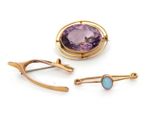 Three brooches: to include a 9ct wishbone brooch stamped 9.375 with Chester assay mark, 1.2g; an oval amethyst brooch, indist