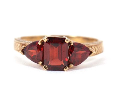 A 9ct garnet ring, set with a step cut garnet to centre and a trillion cut garnet to either side, with scrolled gallery and p