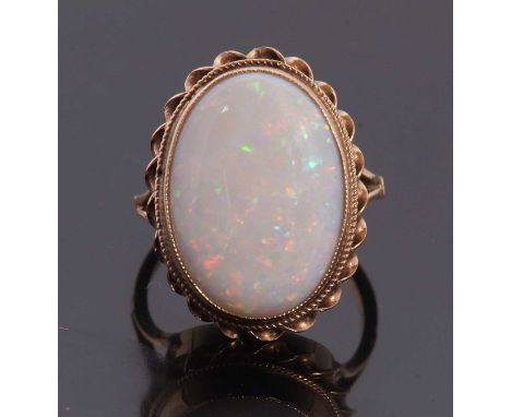 A 9ct opal ring, the oval opal cabochon, collet mounted with rope twist border, with split shoulders and plain band hallmarke