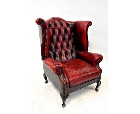A contemporary oxblood leather button pressed wing backed armchair, raised on cabriole supports to pad feet.