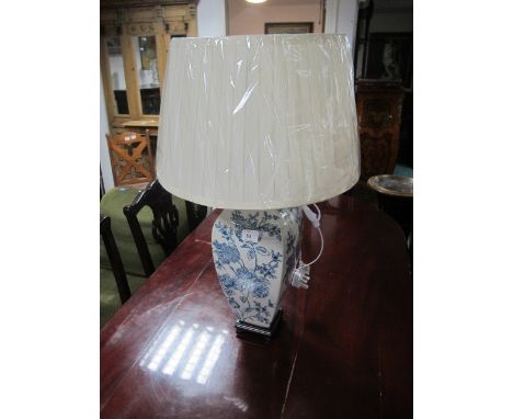 A PORCELAIN TABLE LAMP the white and blue ground decorated with flowerheads and foliage raised on a hardwood base with pleate