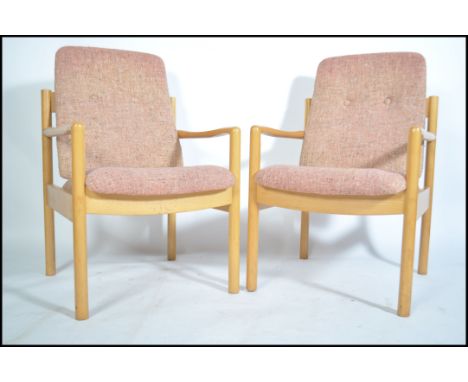 A pair of 20th century Ercol staff chairs. Light beech wood turned construction with shaped elbow rests having upholstered se