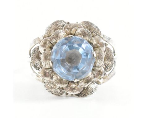 A vintage white metal and synthetic spinel dress ring. The ring in the form of a rose having a round cut pale blue stone set 