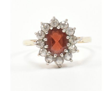 A hallmarked 9ct gold garnet and CZ ring. The ring being set with an oval cut garnet with a halo of CZ. Hallmarked London Bir