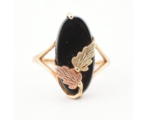 A 10ct gold and onyx dress ring. The ring set with an oval cut onyx embellished bi-colour gold leaf decoration to bifurcated 