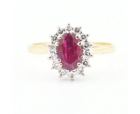 A hallmarked 18ct gold, ruby and diamond halo ring. The ring having an oval cut ruby to the centre encompassed by a cluster o