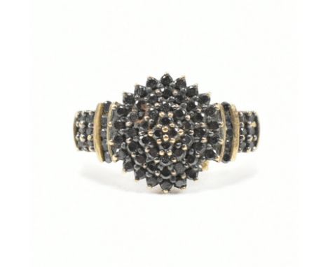 A hallmarked 9ct gold and black diamond cluster ring. The ring set with a central cluster of black diamonds having black diam