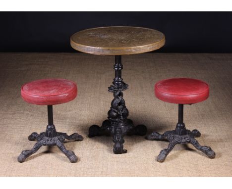 A Small Cast Iron Pedestal Table and Two Stools: The table having a circular top clad in embossed brass on a stop fluted cent