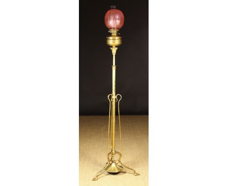 A Brass Oil Lamp with etched cranberry glass shade on a floor standing height adjustable Art Nouveau stand with tripod base a