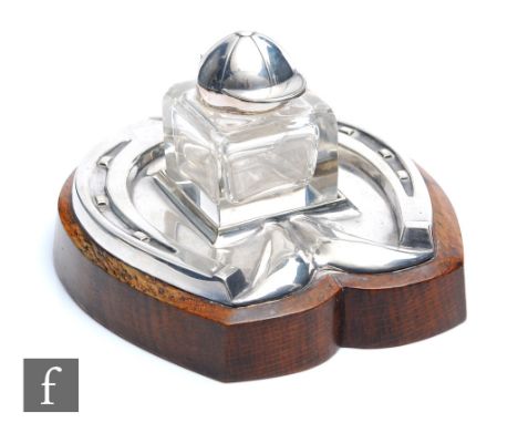 An early 20th Century silver plated ink well and stand, the stand modelled as a horse shoe and the square glass well with a s