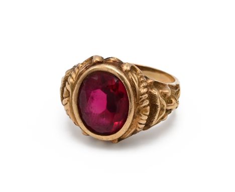 An 18ct yellow gold gem set gentleman's ring, set with a large oval mixed cut synthetic ruby, the shoulders cast with masks, 