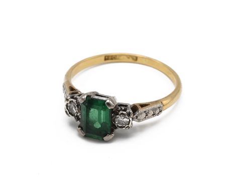 An 18ct yellow gold emerald and diamond ring, the rectangular mixed cut emerald approximately 7mm x 5mm x 3.45mm, flanked by 