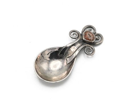 A George V silver and enamel caddy spoon, with a hammered fig-shaped bowl, the tapering handle terminating in scrolling wirew