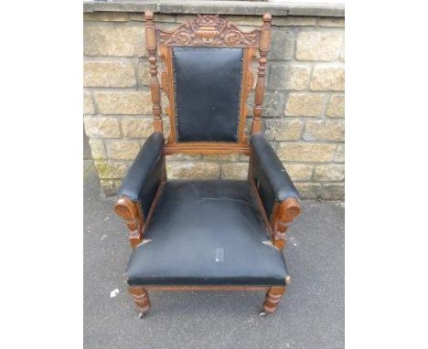 A good early 20th Century light oak library elbow chair with turned top finials, the top rail carved with a neo-classical urn