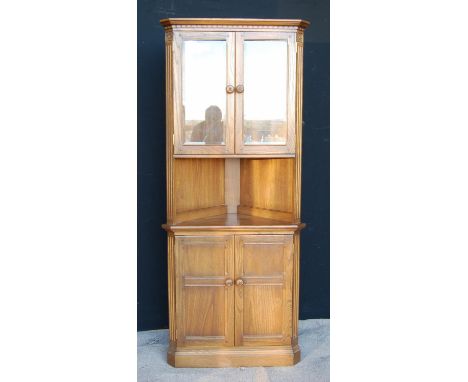 Ercol corner cupboard, the projected moulded cornice over glazed doors, open shelf, panelled doors and raised on a plinth bas