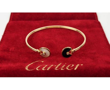 A CARTIER 18CT GOLD BANGLE, set with mother-of-pearl and black onyx roundel terminals, each bearing a central round brilliant