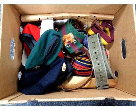 A box containing assorted army belts and berets bearing badges.