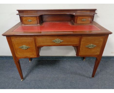 An Edwardian inlaid mahogany knee-hole writing desk on raised legs with a red leather inset panel.