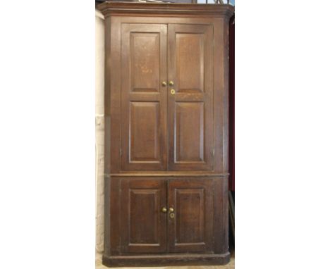 A George III oak full height corner cupboard, with two large panelled doors above two smaller panelled doors enclosing an int