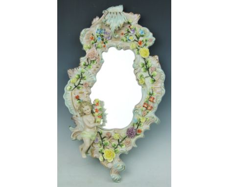 A German porcelain wall mirror, of Rococo design, florally encrusted throughout and modelled with a cherub, 47cm, with a Germ