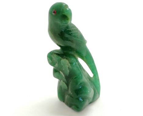 Oriental hand carved figure of a parrot on a rock in green jadeite/jade and has two rubies for eyes. 9cm high. Has natural fl