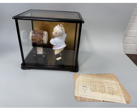 A JAPANESE CERAMIC MODEL OF A CHILD HITTING A DRUM, IN GLASS CASE38cm x 34cm x 28cm