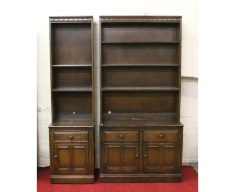 An Ercol dark oak open bookcase over cupboard base along with similar slender example.