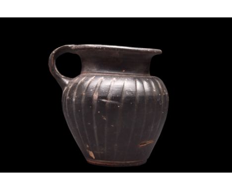 Ca. 400-300 BC.A black glazed mug featuring an elegant inverted pear-shaped body with incised vertical grooves around the bod