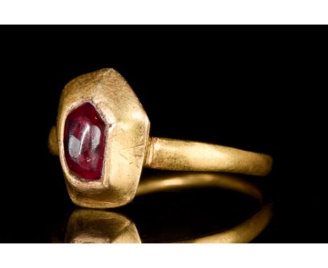 Ca. 1400 AD.A gold ring with a slender round hoop, slightly widening to a plano-convex bezel with inset ruby cabochon. Size: 