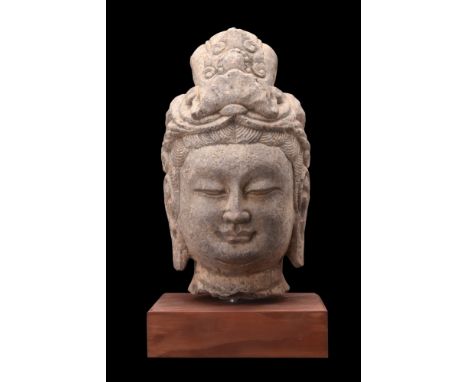 Ca. 581-618 AD.A stone head of Buddha with elaborate coiffured hair curls under a richly ornamented headdress. He is characte