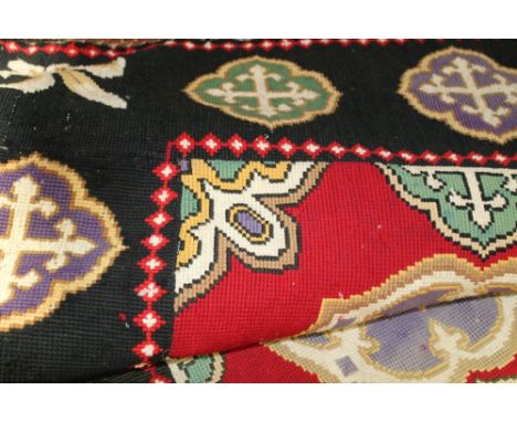 Large tapestry floor covering brightly coloured motifs on black ground with fleur de lis and eccesiastica; crosses.