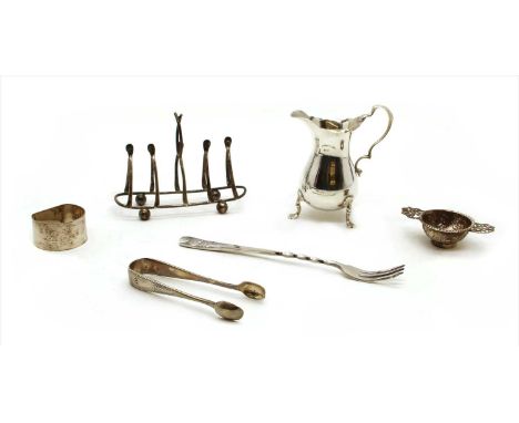 A collection of silver items to include a cream jug , tongs, toast rack, napkin ring, etc (Qty.)