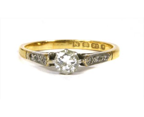 A gold single stone diamond ring, with a brilliant cut diamond, claw set to tapered shoulders, grain set with eight cut diamo