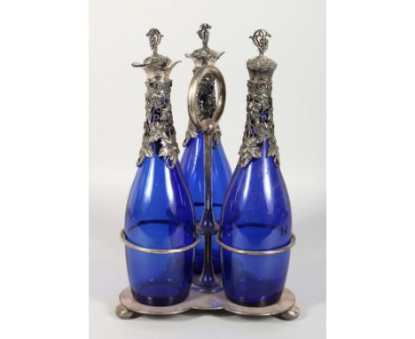 A PLATED THREE BOTTLE DECANTER SET, with "BRISTOL BLUE" DECANTERS, having grape and vine mounts. 14ins high.
