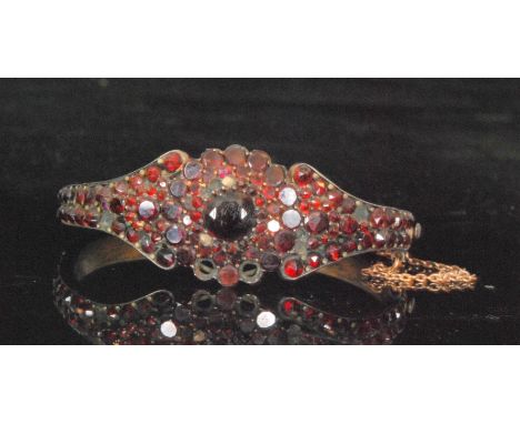 A 19th to early 20th Century yellow metal Bohemian garnet hinged bangle, the whole encrusted with rose cut garnets and centre