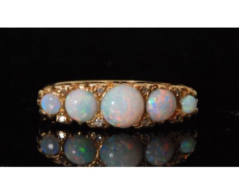 A later 20th Century 18ct hallmarked opal and diamond ring five graduated opals spaced by pairs of diamonds to a scroll head 