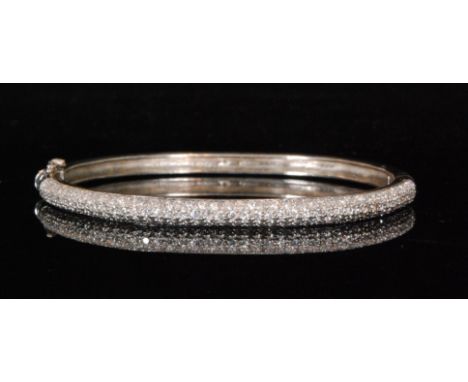 A modern white metal and diamond encrusted hinged bangle with figure of eight safety catch, weight 18g, unmarked.  
