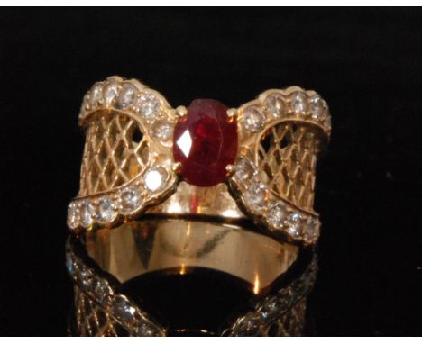 An 18ct ruby and diamond ring, central claw set oval ruby flanked by horseshoe set diamond shoulders spaced by lattice work f