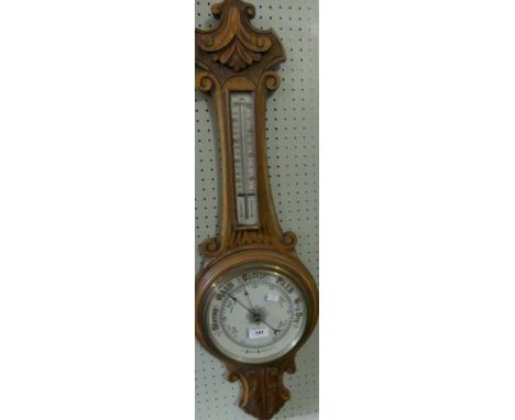 A late 19th/early 20th Century aneroid barometer/thermometer in carved oak case.
