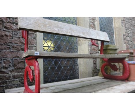 A garden bench with weathered oak plank seat and back rail raised on decorative heavy cast iron serpent supports with painted