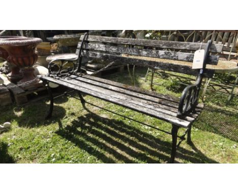 A two seat garden bench with weathered timber slatted seat and back raised on a pair of decorative cast end supports with sim