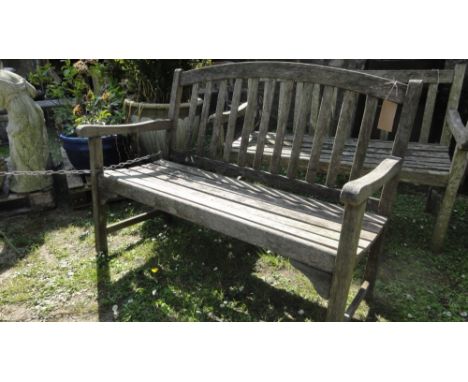 A weathered contemporary teak two seat garden bench with slatted seat and back beneath an arched rail.