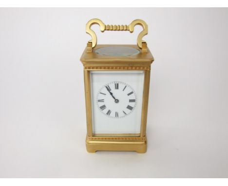 French oval brass carriage clock, with enamelled mask and bevelled glass, upon ball feet, 11.5 cm high