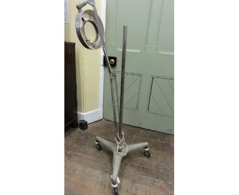 An industrial medical lamp upon a good industrial tripod base fitted with castors.