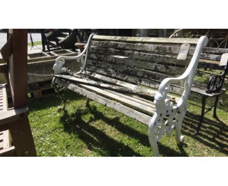 A two seat garden bench with weathered wooden slatted seats and combined back raised on a pair of decorative painted cast alu