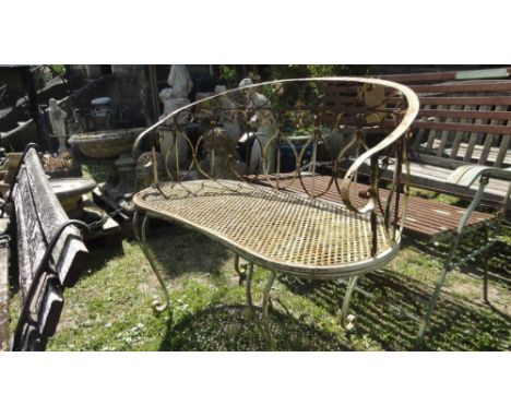 A weathered light steel framed two seat garden bench with decorative scroll work back beneath a curved and scrolled rail over